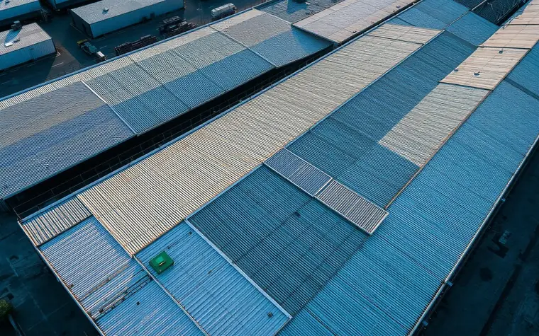 Aerial view of a large industrial warehouse roof with coated and uncoated sections